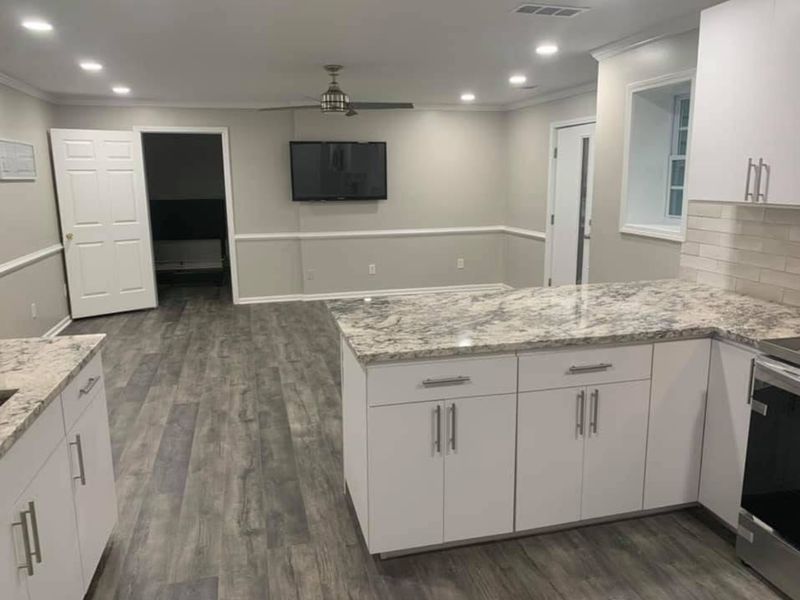 Kitchen peninsula with stone counters opening to a living room with a wall-mounted TV
