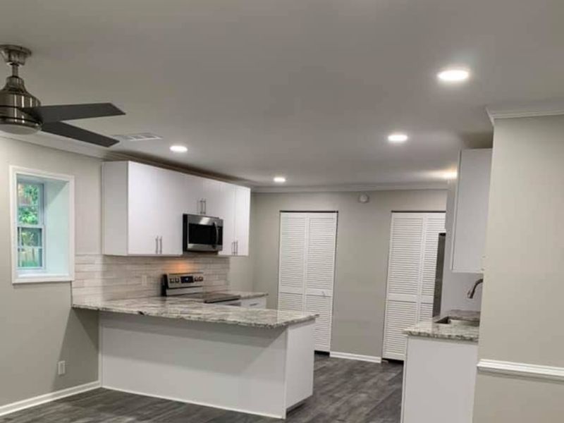 Kitchen with white cabinets, a stainless microwave and range, and a stone-top peninsula